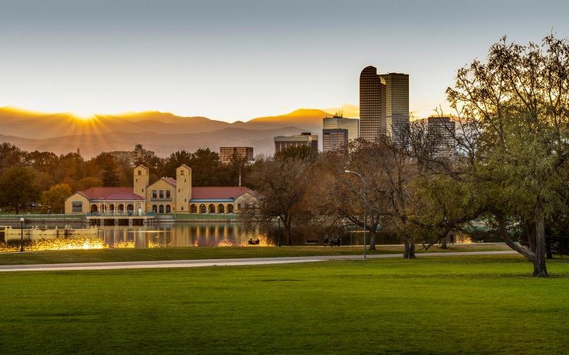 a large green field with trees and buildings in the background